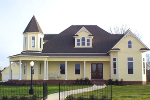 A Victorian-style spec home with a turret and wraparound porch